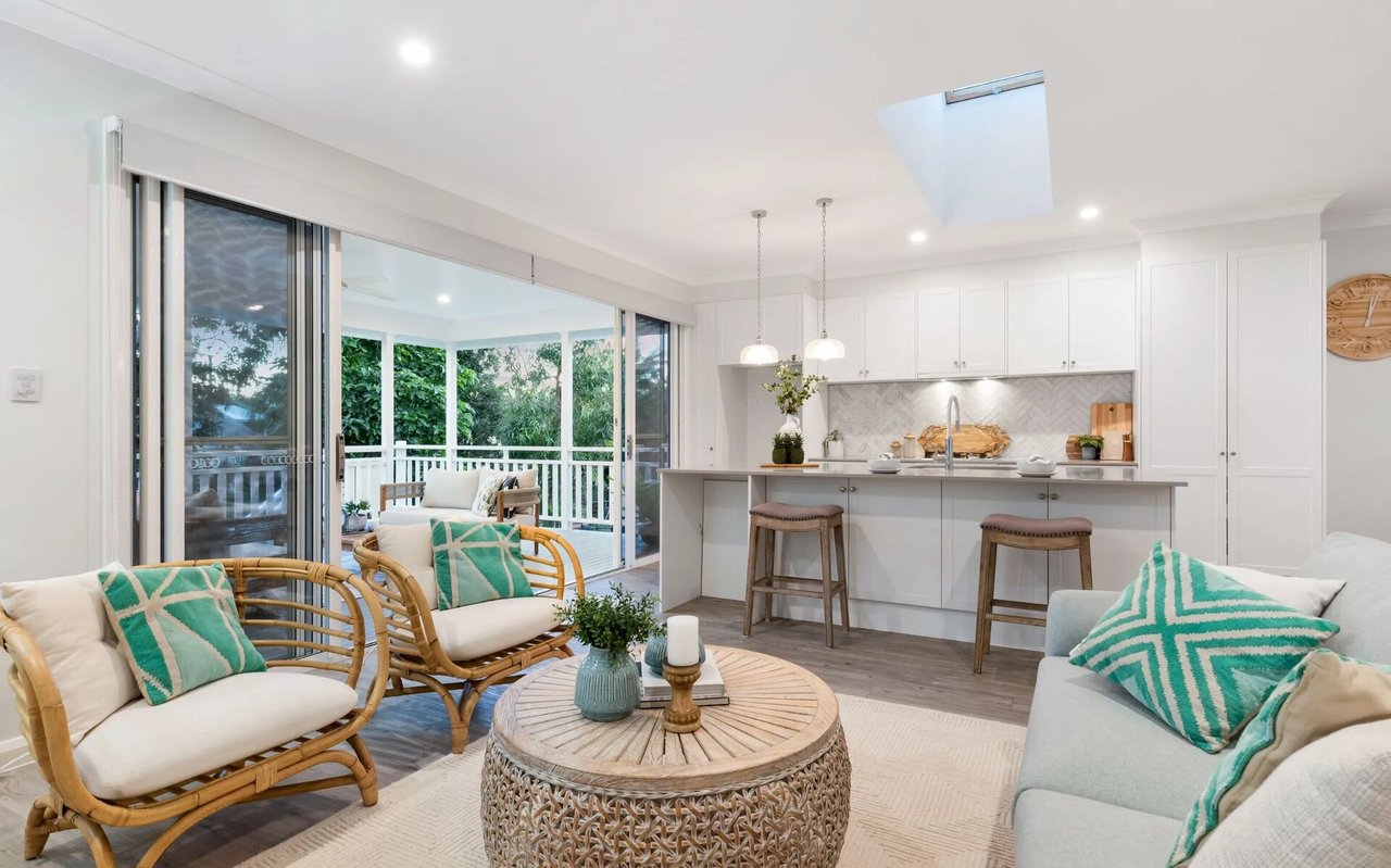 Open-plan living room and kitchen with rattan seating and sliding doors to a leafy deck.