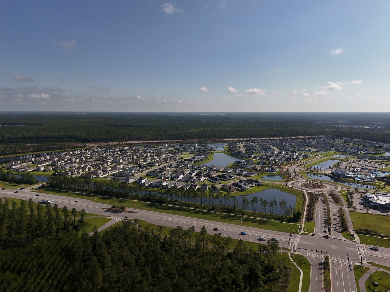 Aerial view of a residential neighborhood with ponds, landscaped roads, and woods.