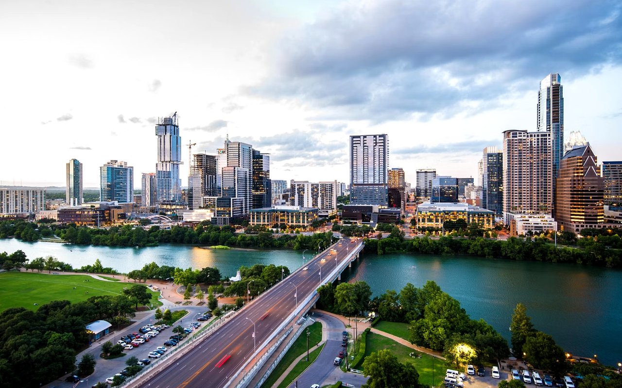 Downtown Austin skyline across Lady Bird Lake, with a bridge and parkland in the foreground.