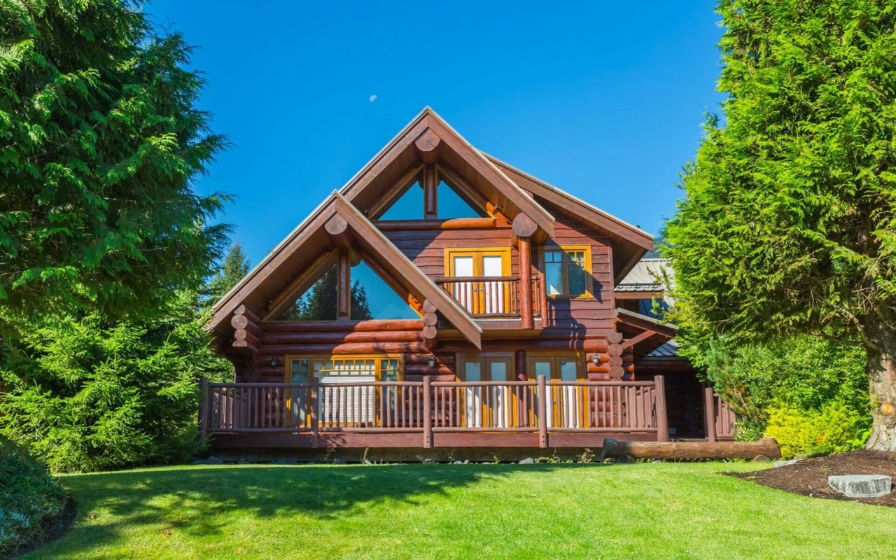 Log cabin with timber gables, a front deck, and an upper balcony among evergreen trees.