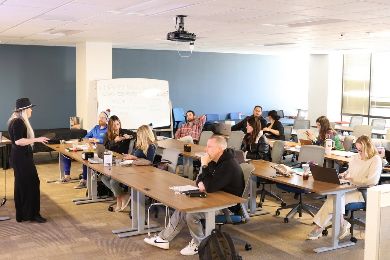 Real estate agents attend a training session as a presenter speaks beside a whiteboard.