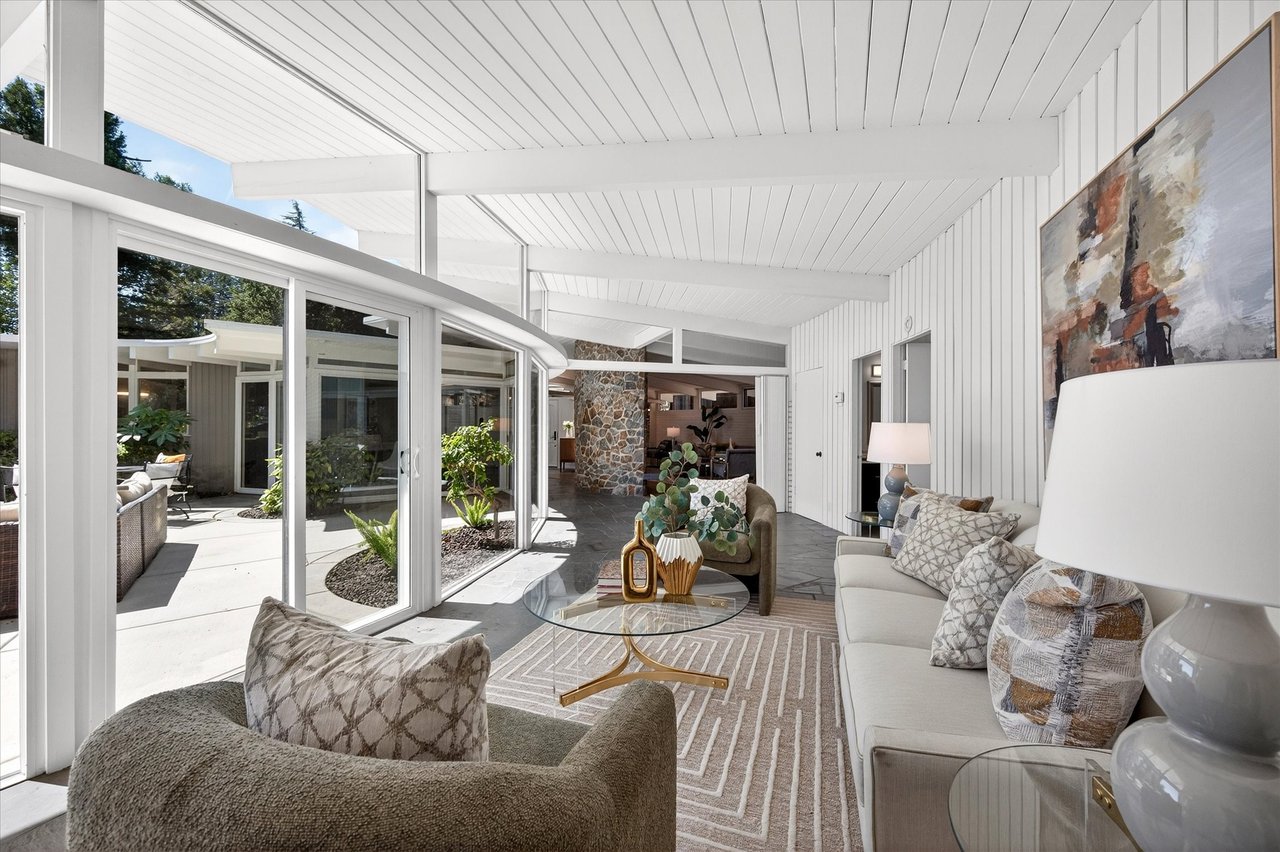 Staged living room with a high white ceiling and glass doors opening to a sunny courtyard.