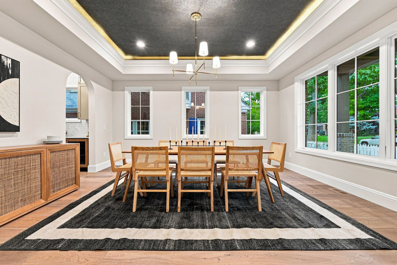 Dining room with a long wooden table, woven chairs, and a dark coffered ceiling with gold trim.