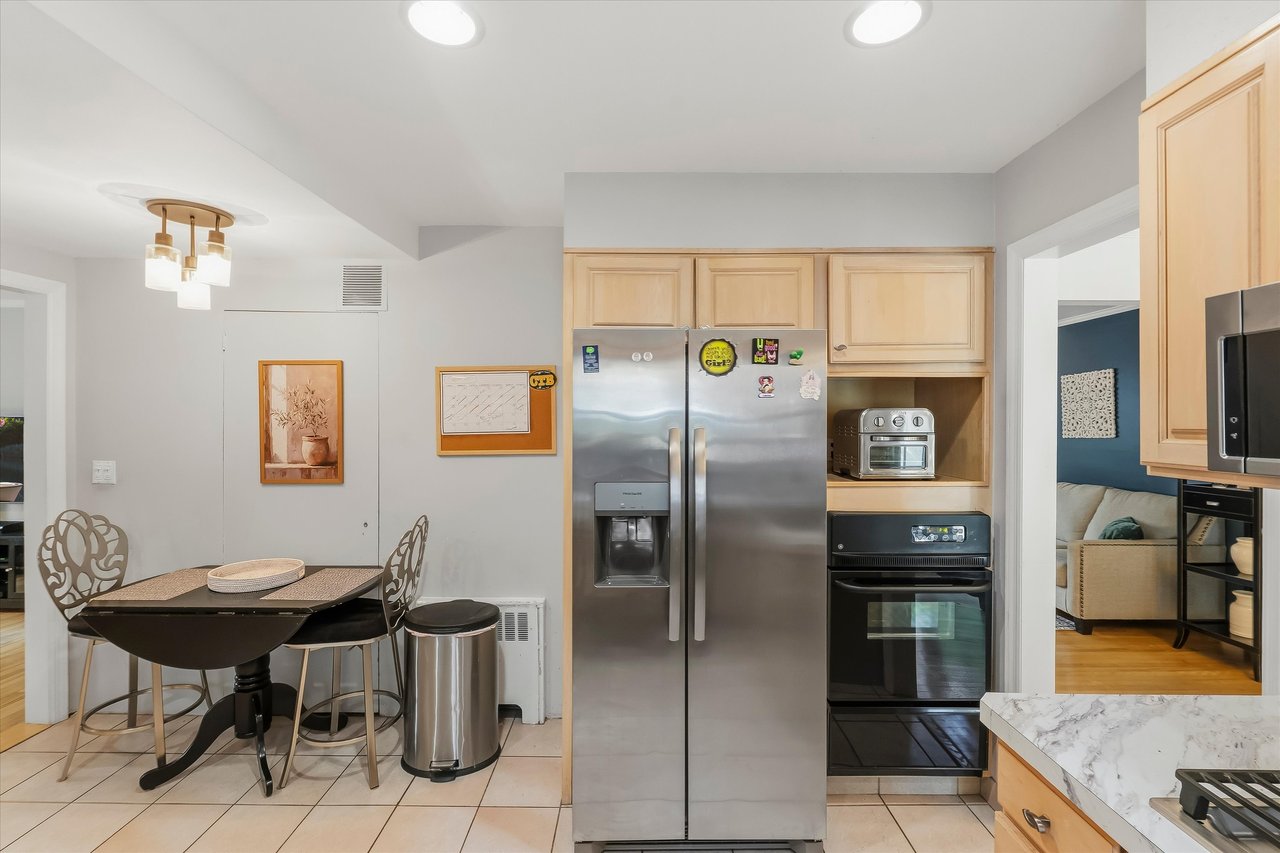 Kitchen with light wood cabinets, stainless steel refrigerator, and a dining table with decorative chairs.