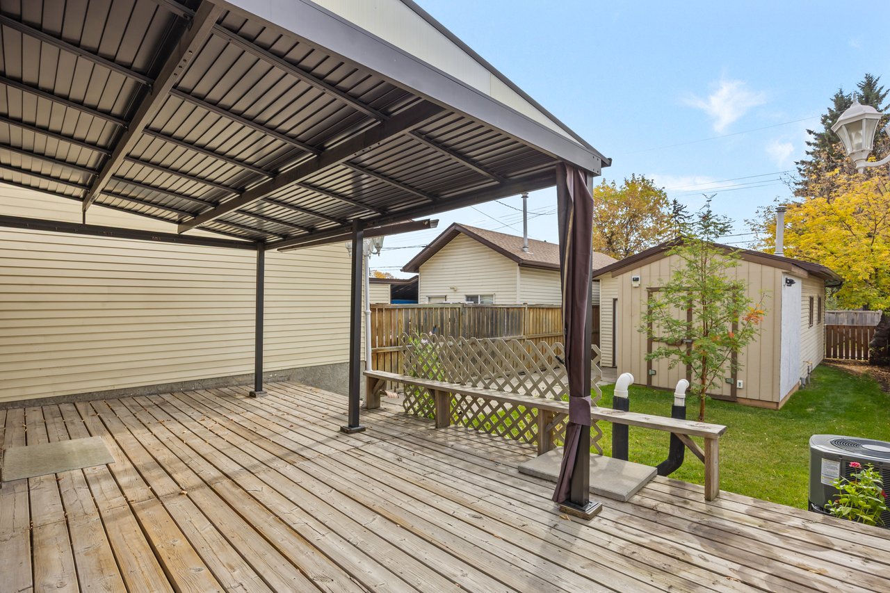 Covered backyard deck with a metal canopy, weathered wood flooring, lattice railing, and built-in bench.