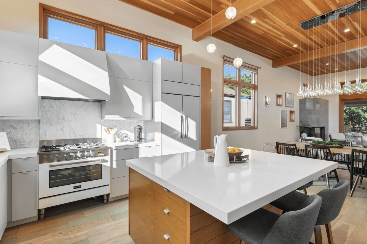 Modern kitchen with a large white island, wood-beamed ceiling, and adjoining dining area