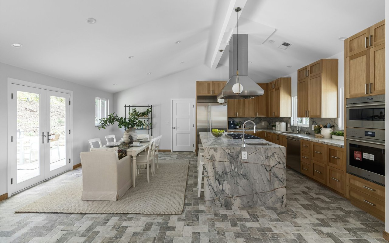 Open-plan kitchen and dining area with a large marble island and warm wood cabinetry.