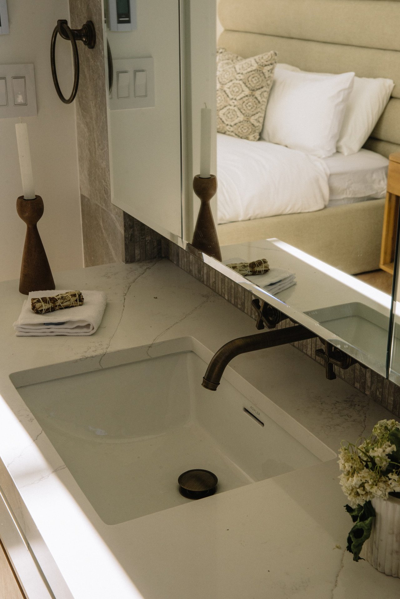 Marble bathroom vanity with a rectangular sink, dark brass faucet, and mirror reflecting a neatly made bed.