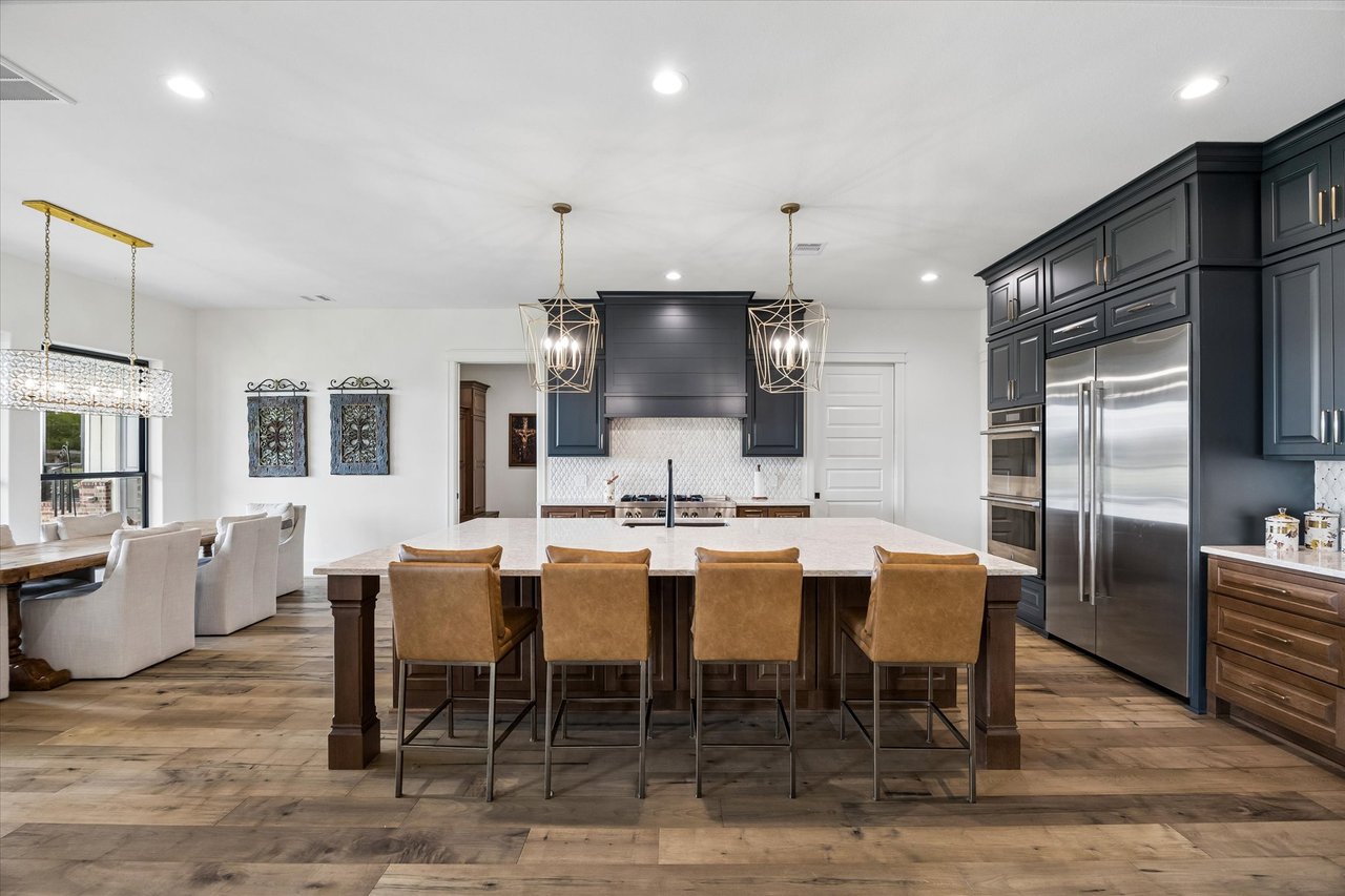 Kitchen with a large marble island, navy cabinets, stainless steel appliances, and four leather bar stools.