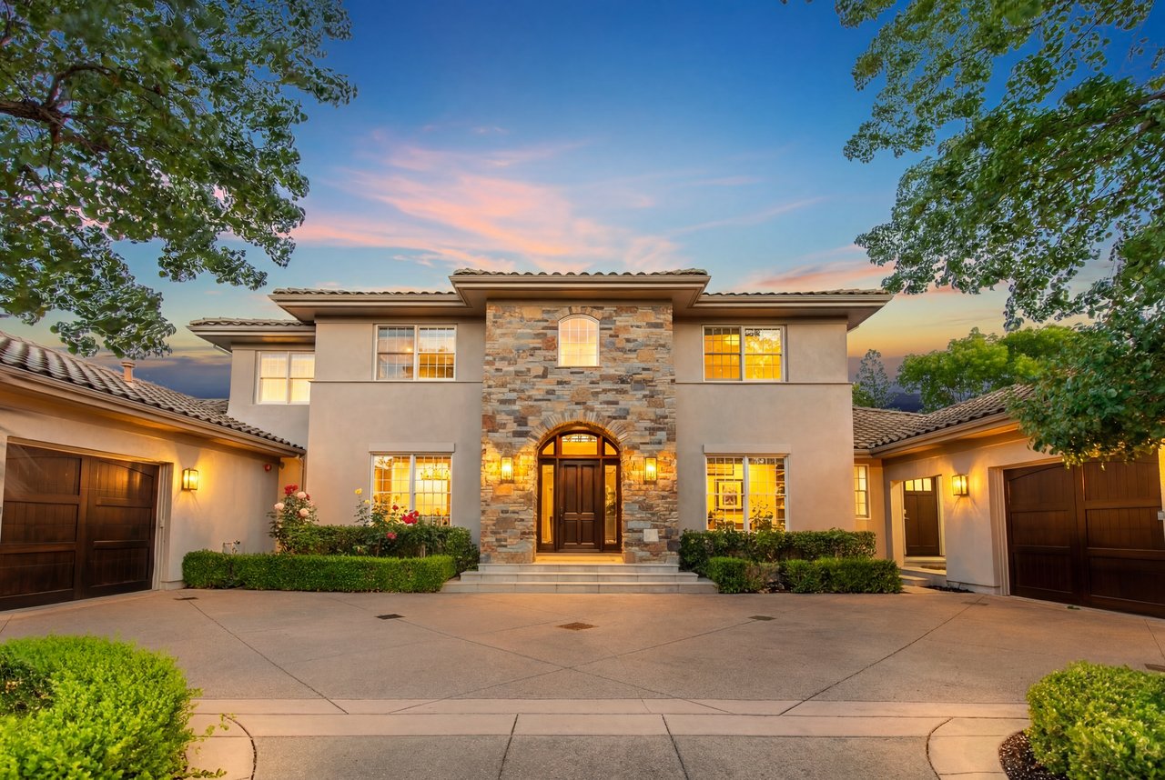 Two-story stucco home with a stone facade, arched entry, attached garages, and warm sunset lighting.