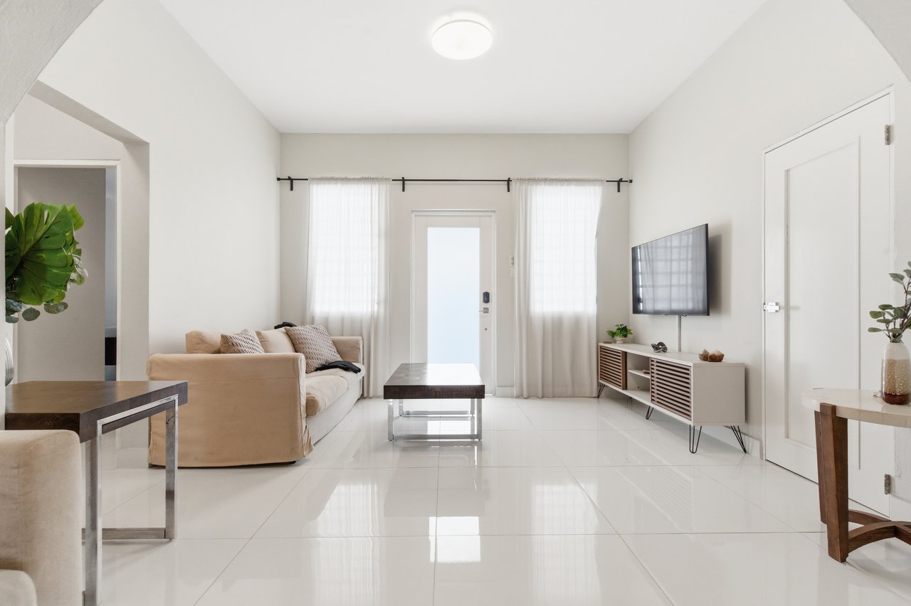 Bright living room with a beige sofa, white tile floors, and a wall-mounted television.