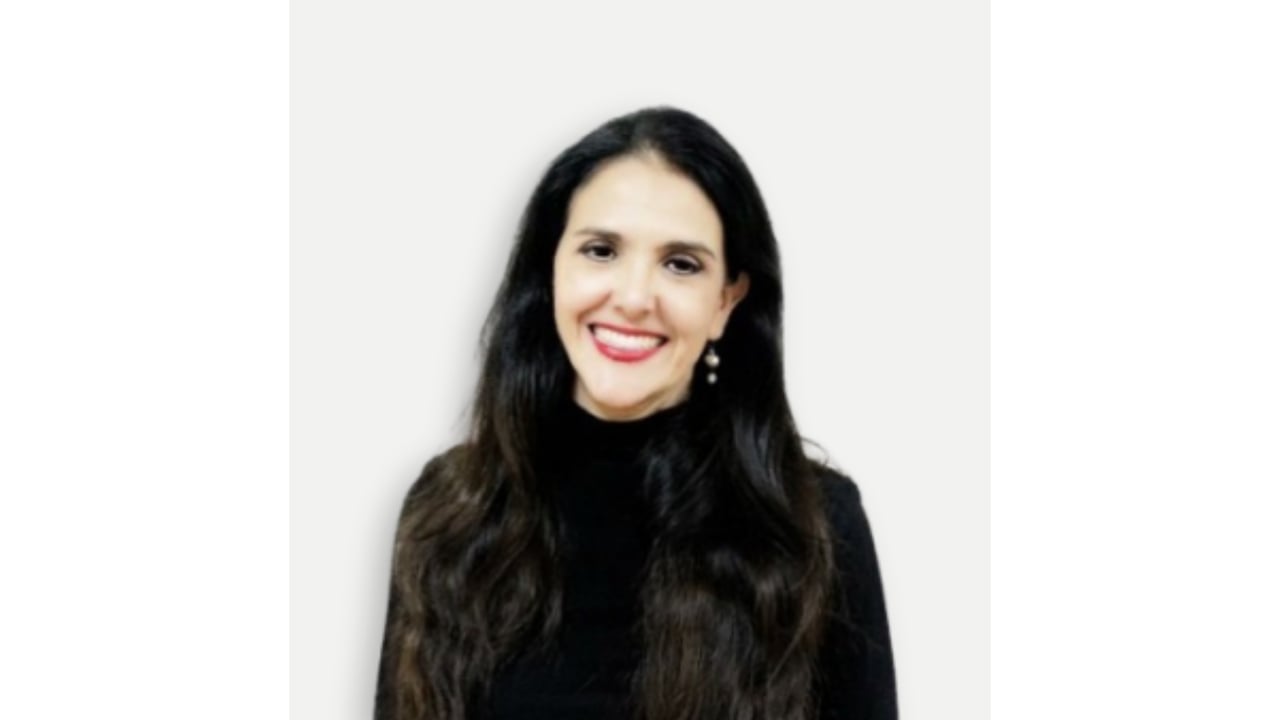 Smiling woman with long dark hair and pearl drop earrings, wearing a black top.