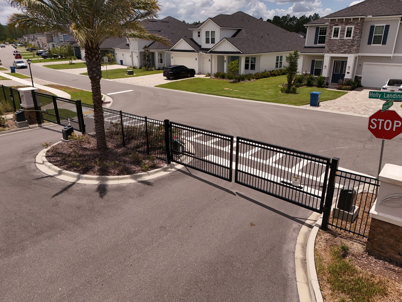 Holly Landing neighborhood entrance with a black metal gate, palm tree, and homes beyond.