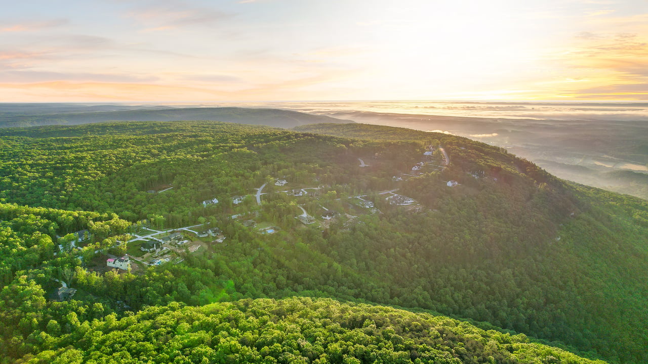 Aerial view of a wooded hillside development with scattered homes and winding roads at sunrise.