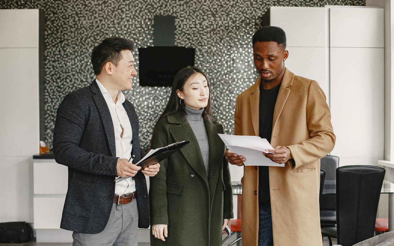 Three people review paperwork together in a modern kitchen.