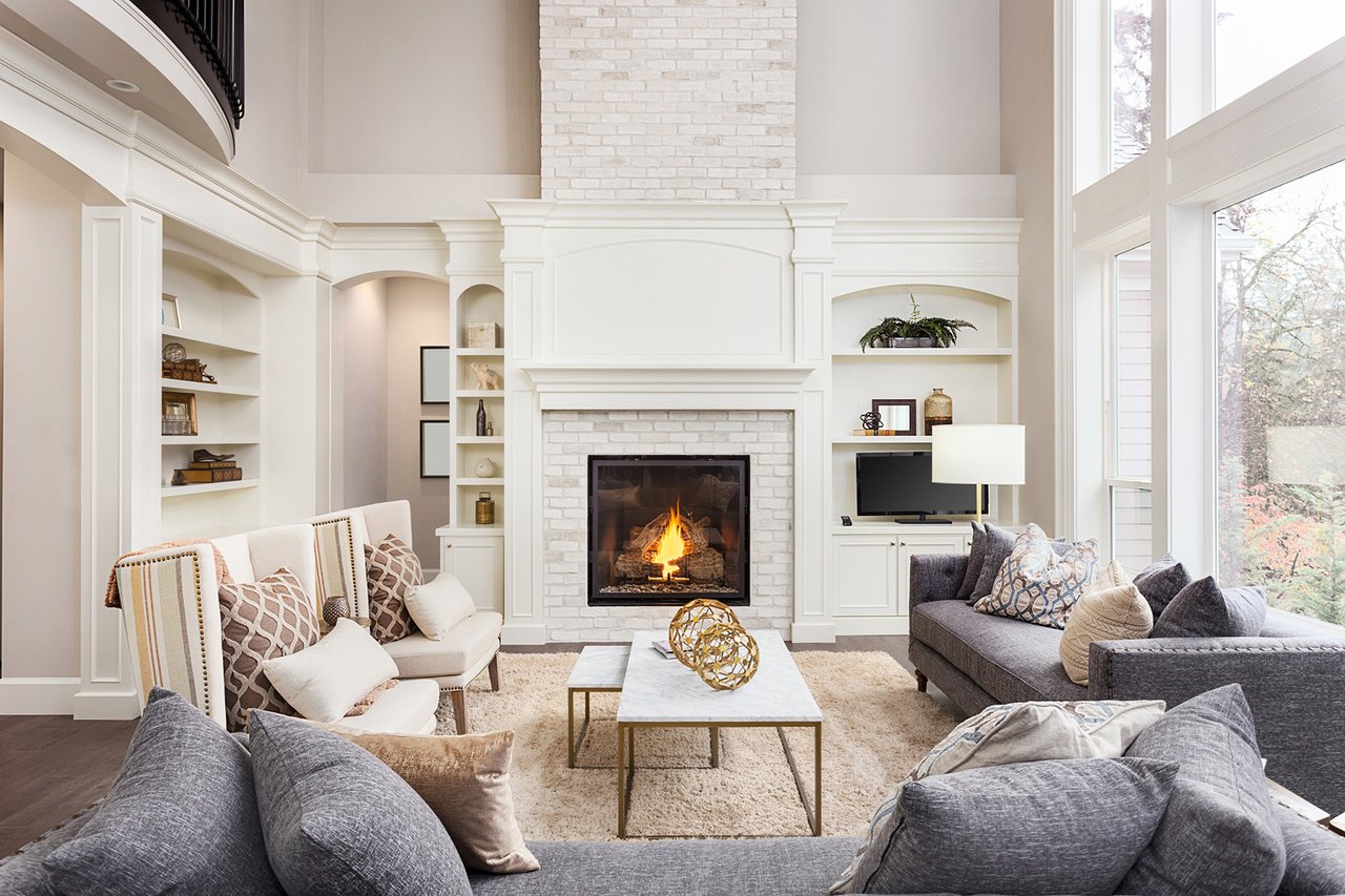 Living room with a white brick fireplace, built-in shelves, high ceilings, and large windows.