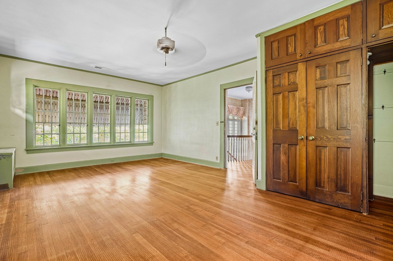 Empty room with polished wood floors, green-trimmed windows, and large paneled wooden closet doors.