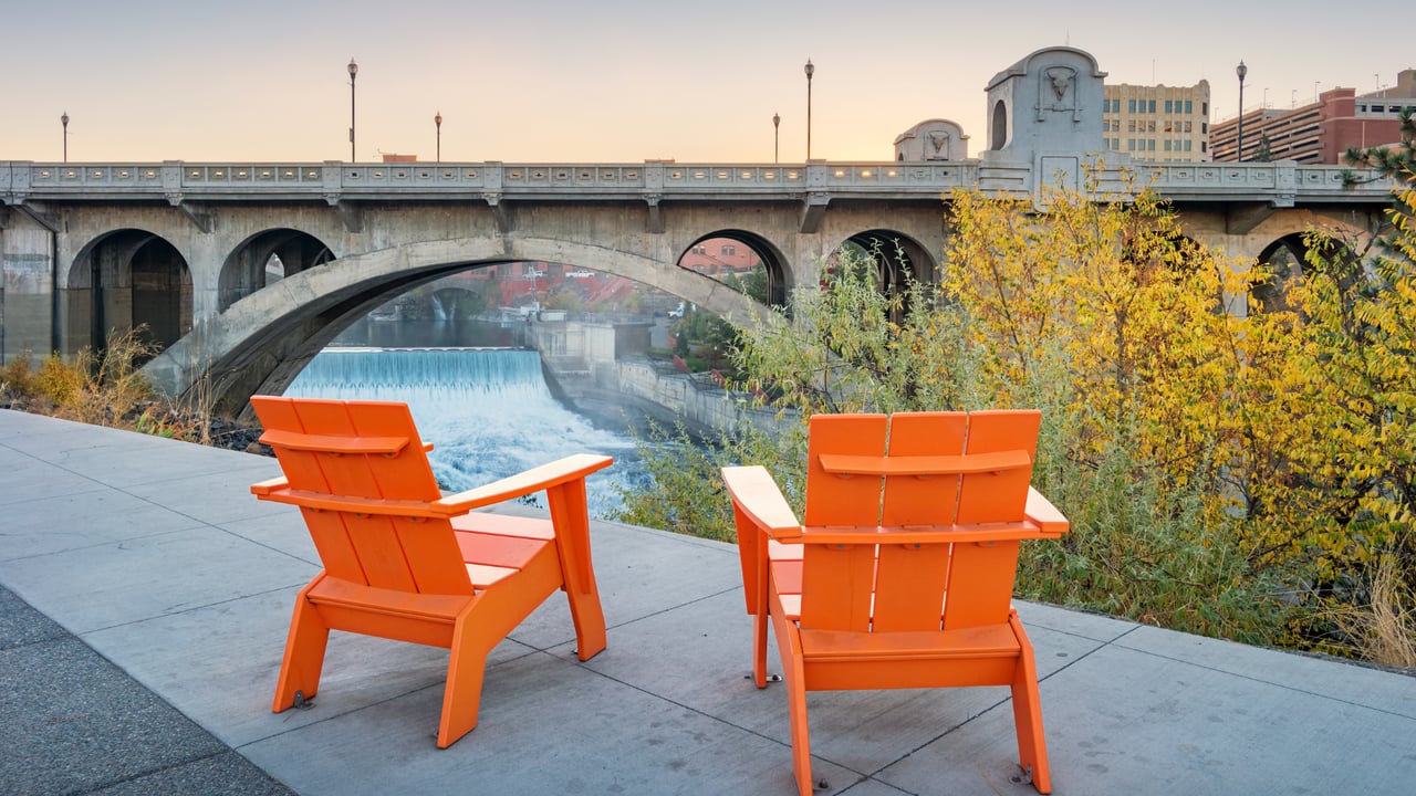 Monroe Street Bridge spans Spokane Falls behind two orange chairs and autumn foliage.