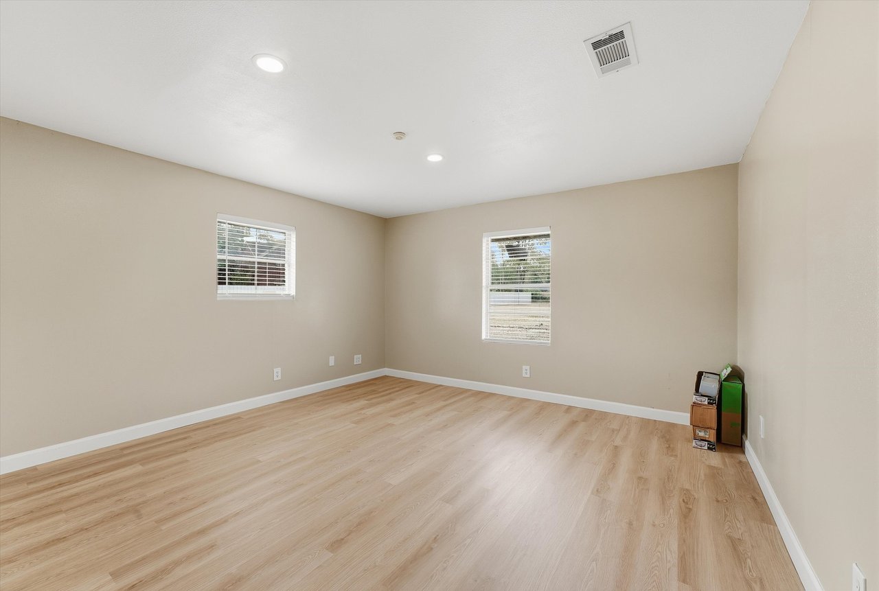 Empty room with light wood-look flooring, beige walls, and two windows with blinds.