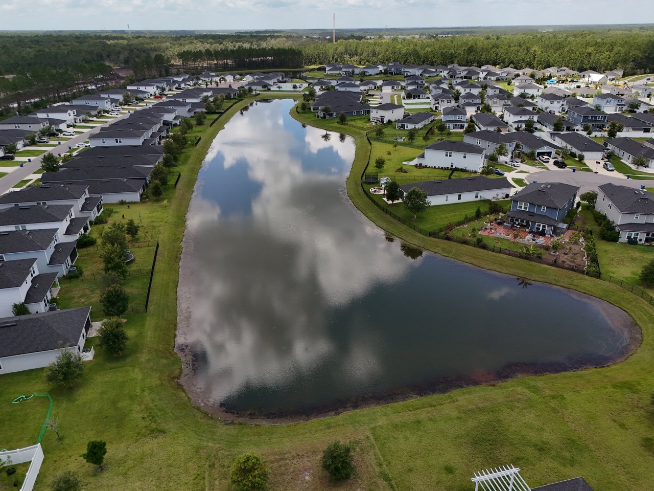 Aerial view of homes surrounding a large pond, with wooded areas in the distance.
