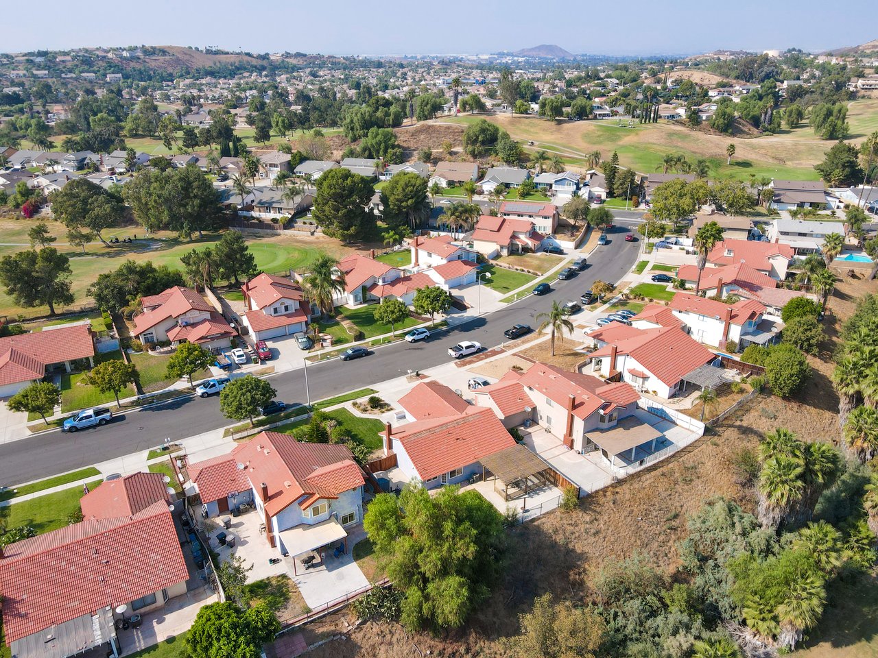 Aerial view of homes with red tile roofs along a residential street, with rolling hills beyond.