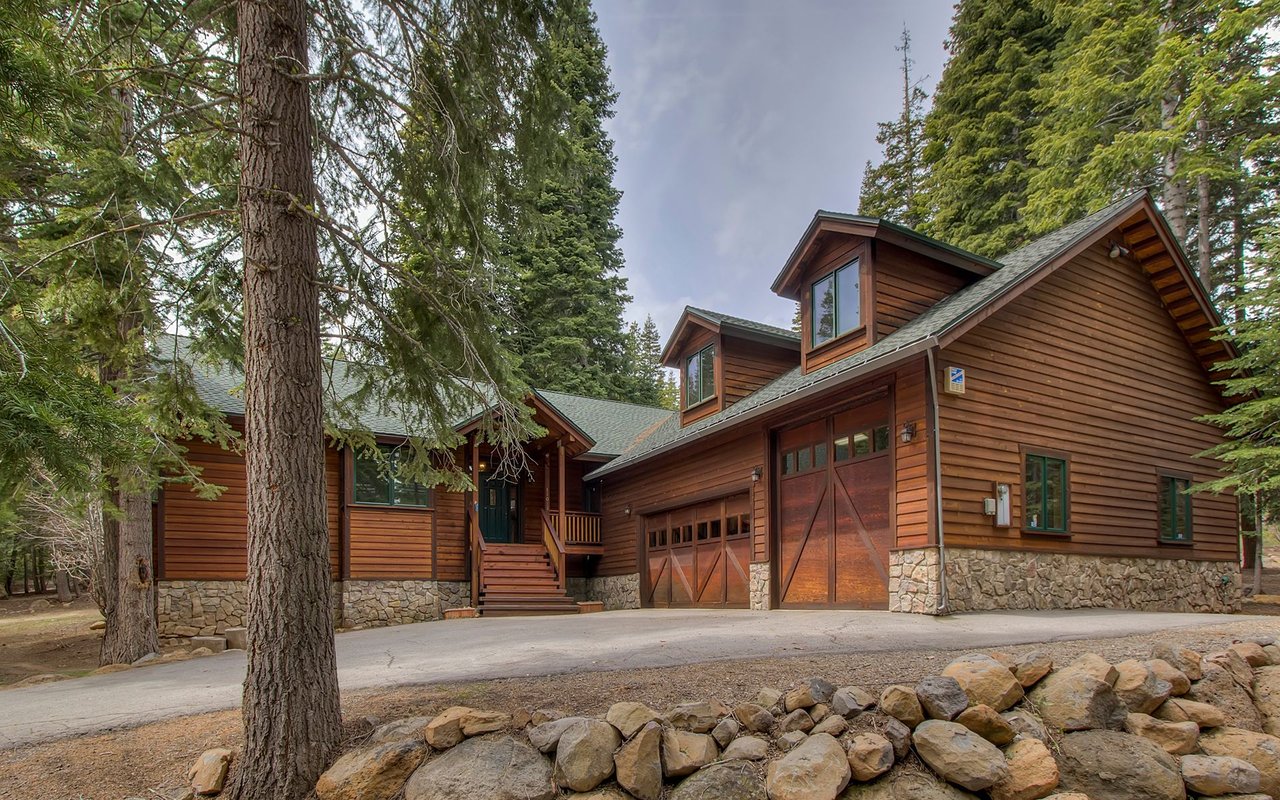 Wood-sided Truckee home with stone foundation and attached garage among tall evergreens.