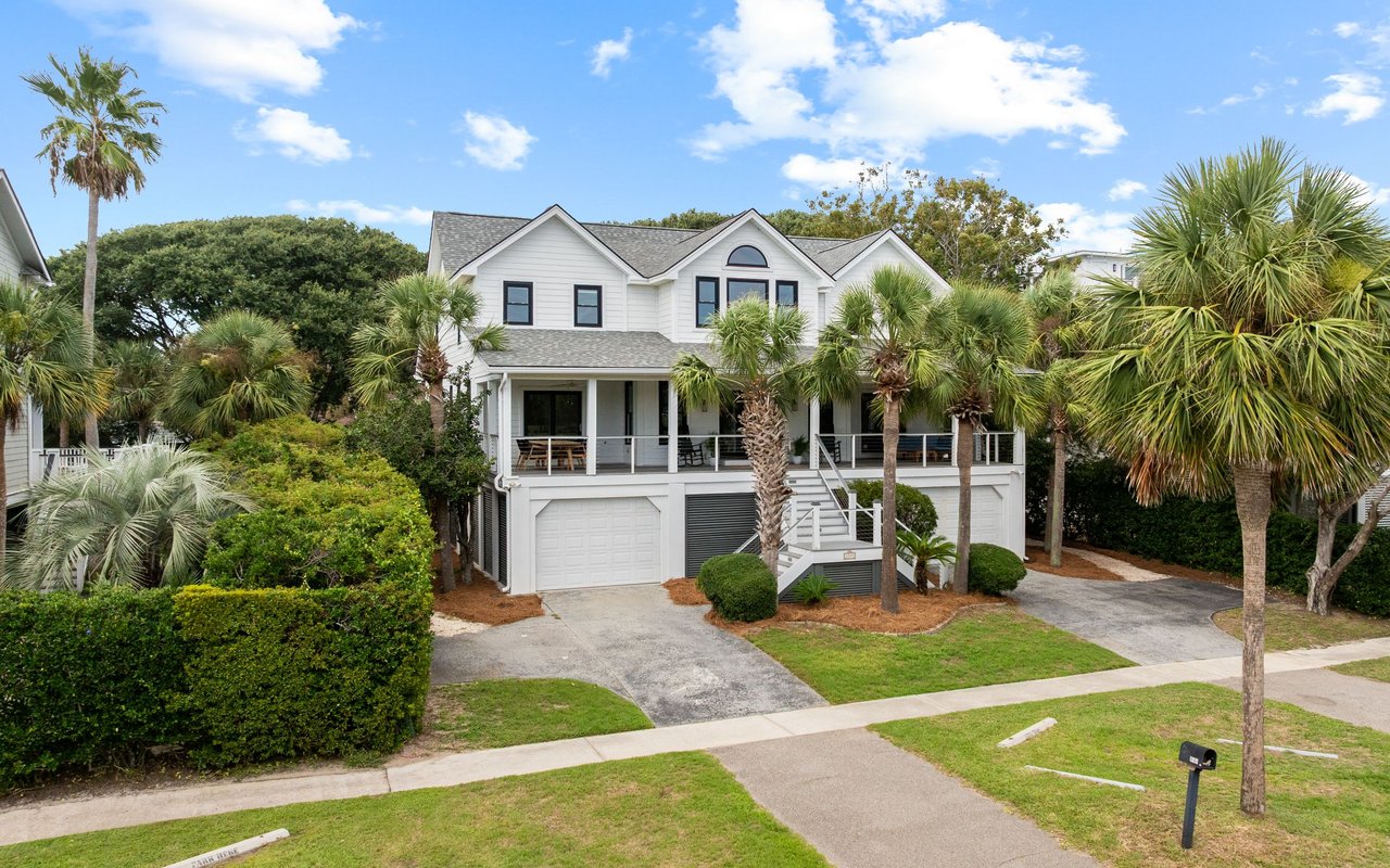 Two-story white coastal home with an elevated porch, garage, and palm trees.