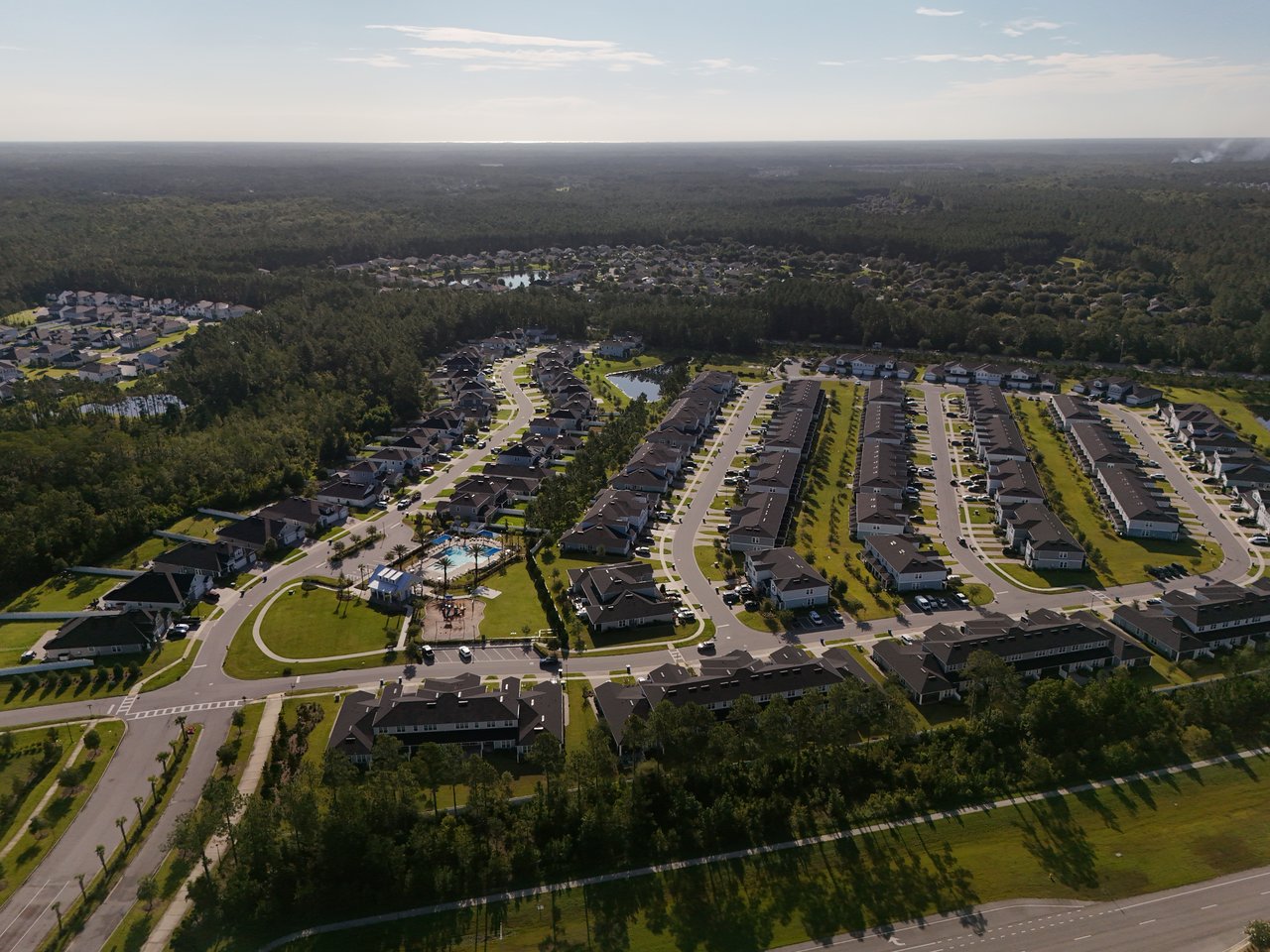 Aerial view of a housing community with curving streets, a pool, and surrounding forest.