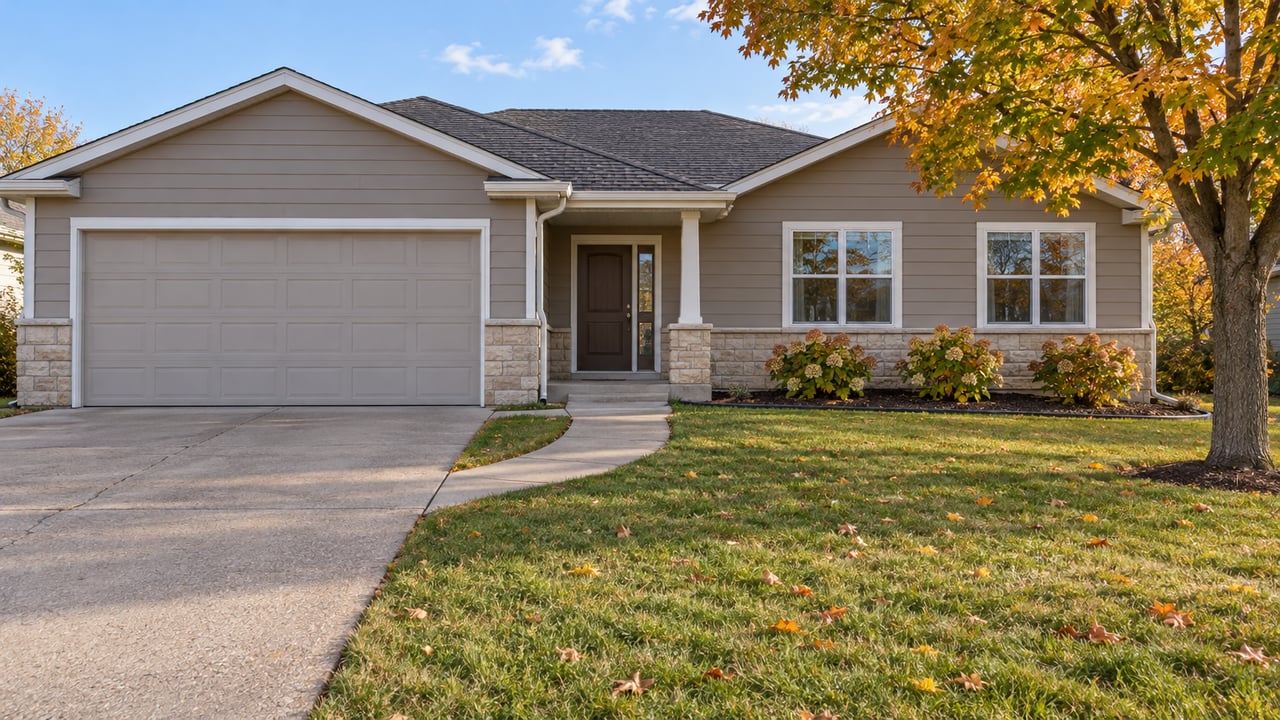 A taupe-sided ranch home with a limestone base, deep front lawn, and an amber-leaved sugar maple in afternoon light.