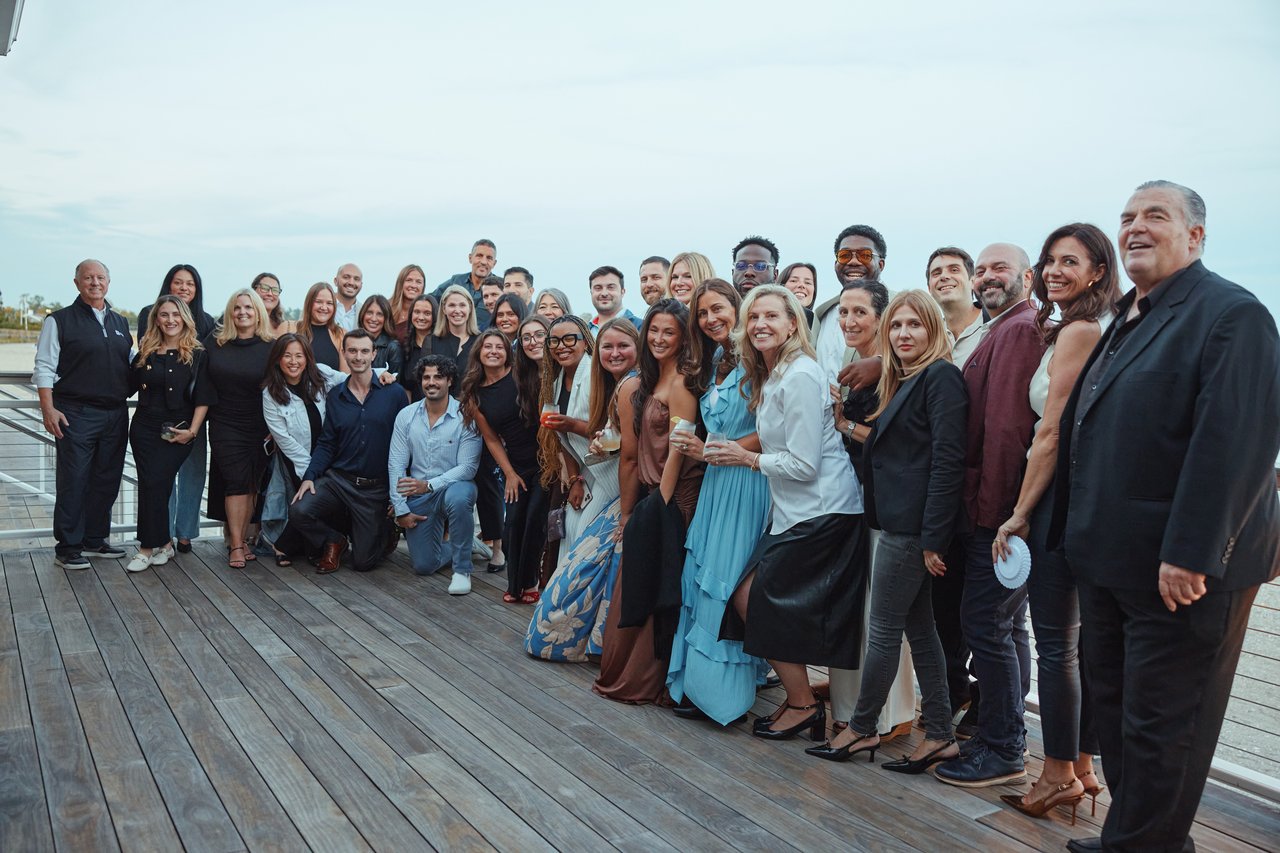 A large group of real estate professionals pose together on a wooden deck.