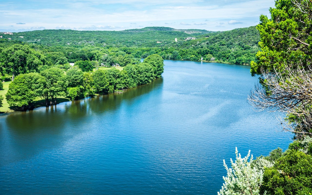 Blue lake bordered by wooded hills, with trees framing the shoreline.