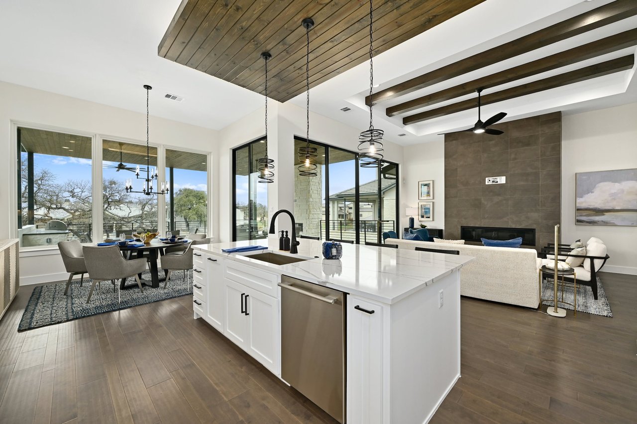 Open-plan kitchen with a large white island, exposed wood ceiling beams, and floor-to-ceiling windows.