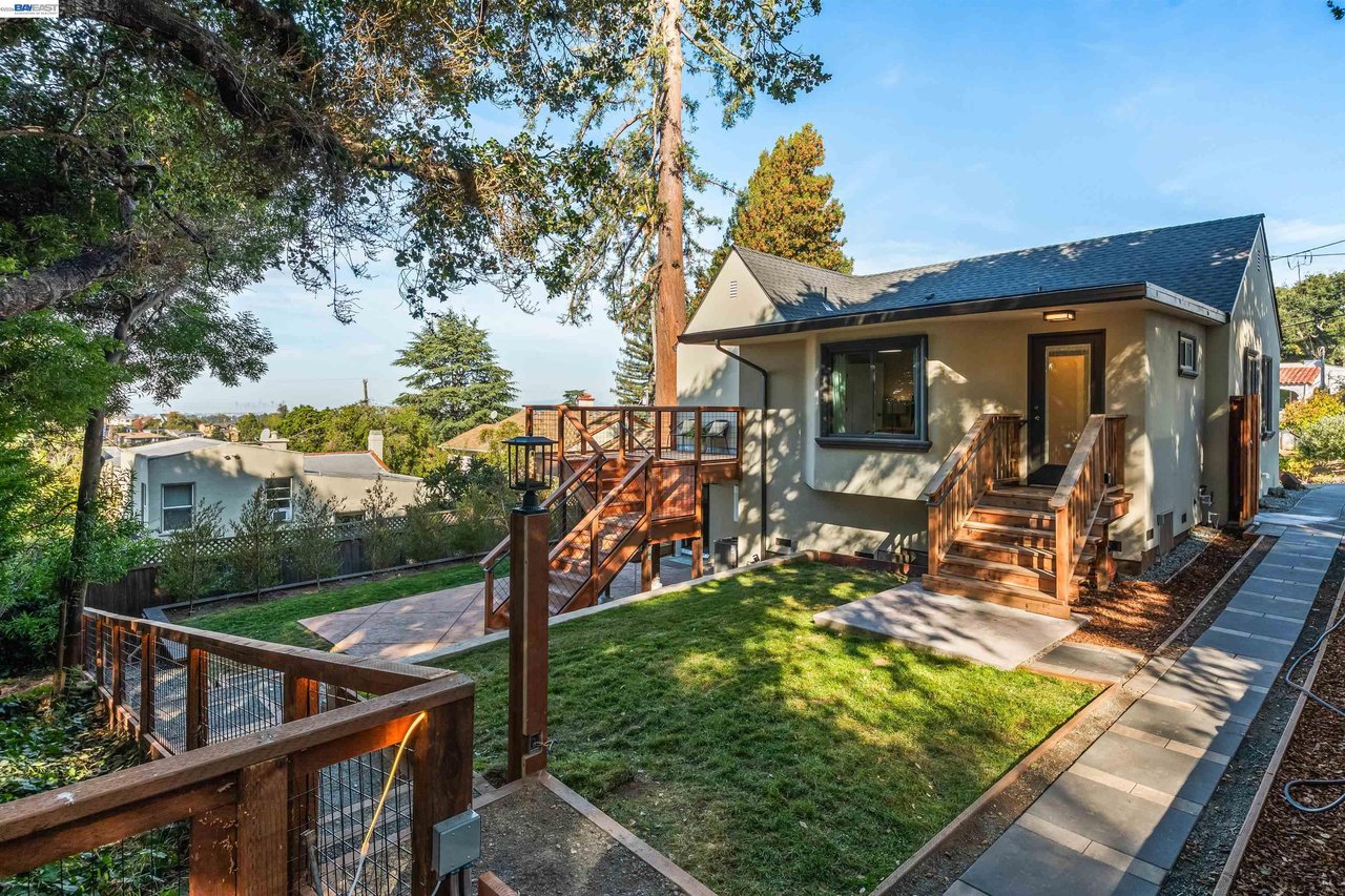 Single-story home with wooden stairs and deck overlooking a fenced grassy yard.