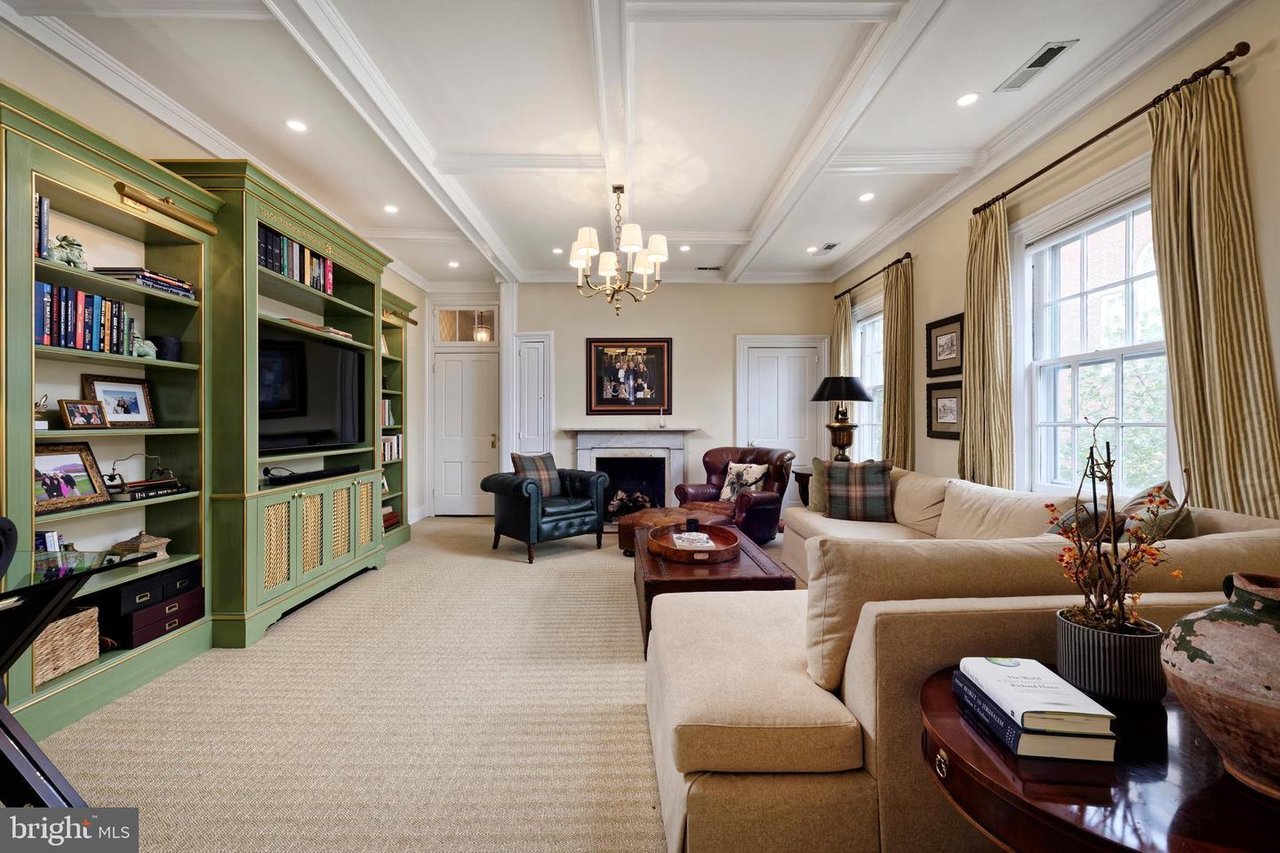 Living room with green built-in bookshelves, a fireplace, coffered ceiling, and large windows.
