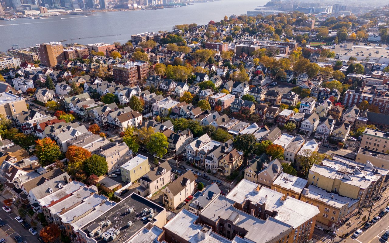 Aerial view of Union City’s homes and autumn trees beside the Hudson River, with Manhattan in the distance.