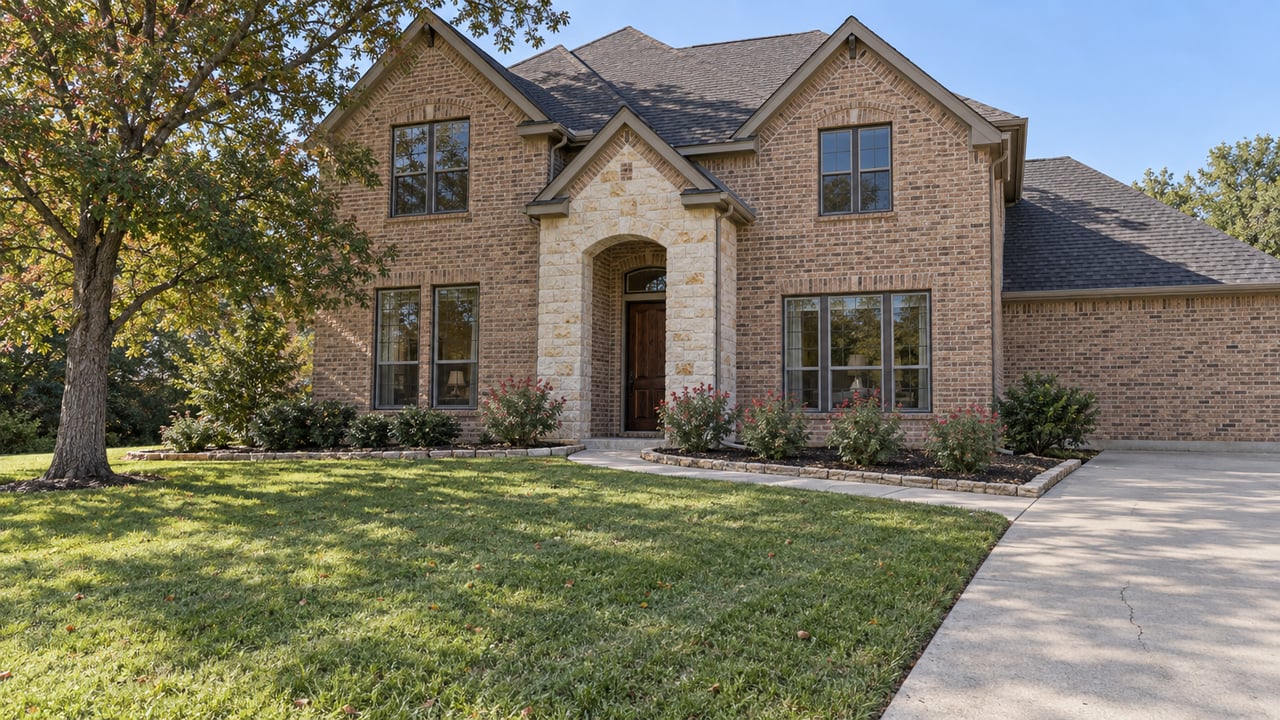 Brick and limestone home with front gables, a deep lawn, a spreading oak and a curved entry walk in clear daylight.