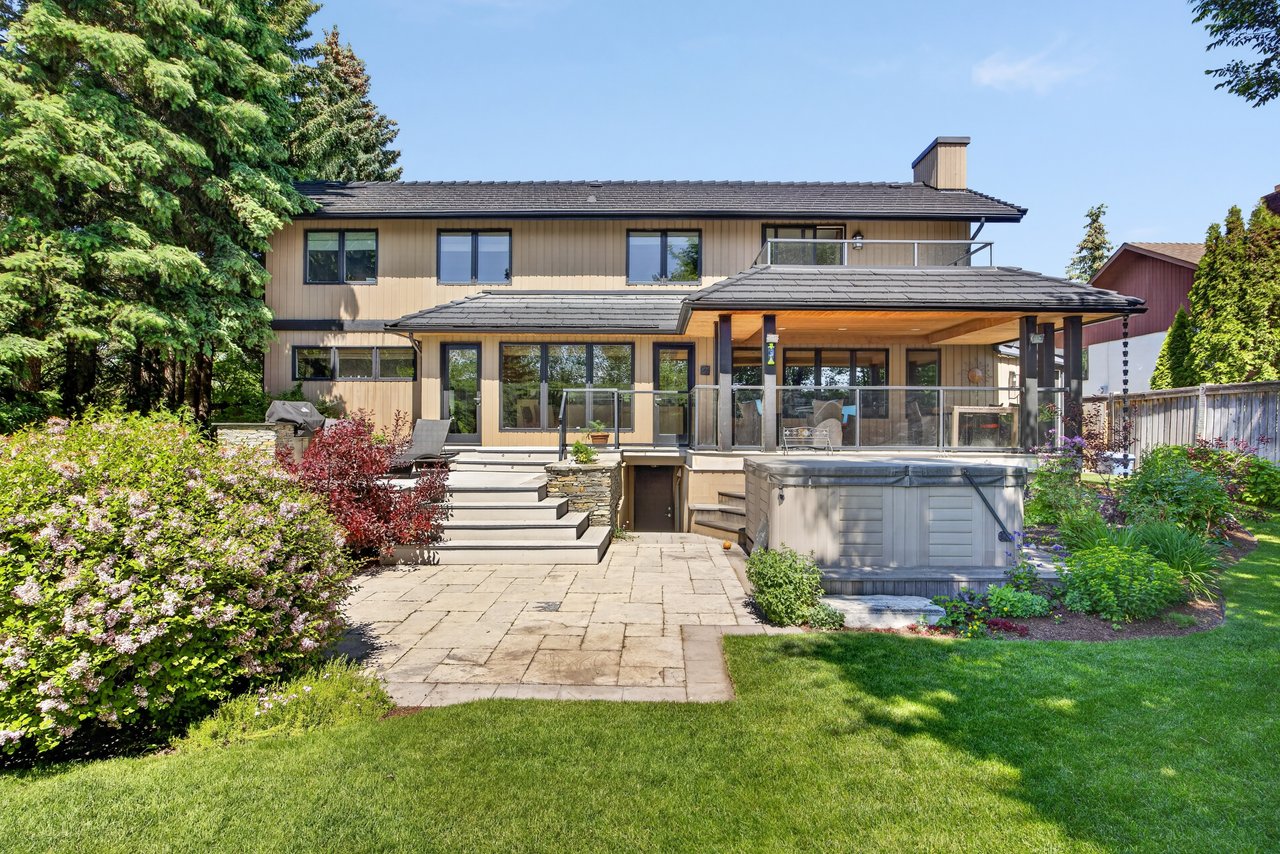 Two-story home with a covered patio, stone terrace, and raised hot tub in a landscaped backyard.