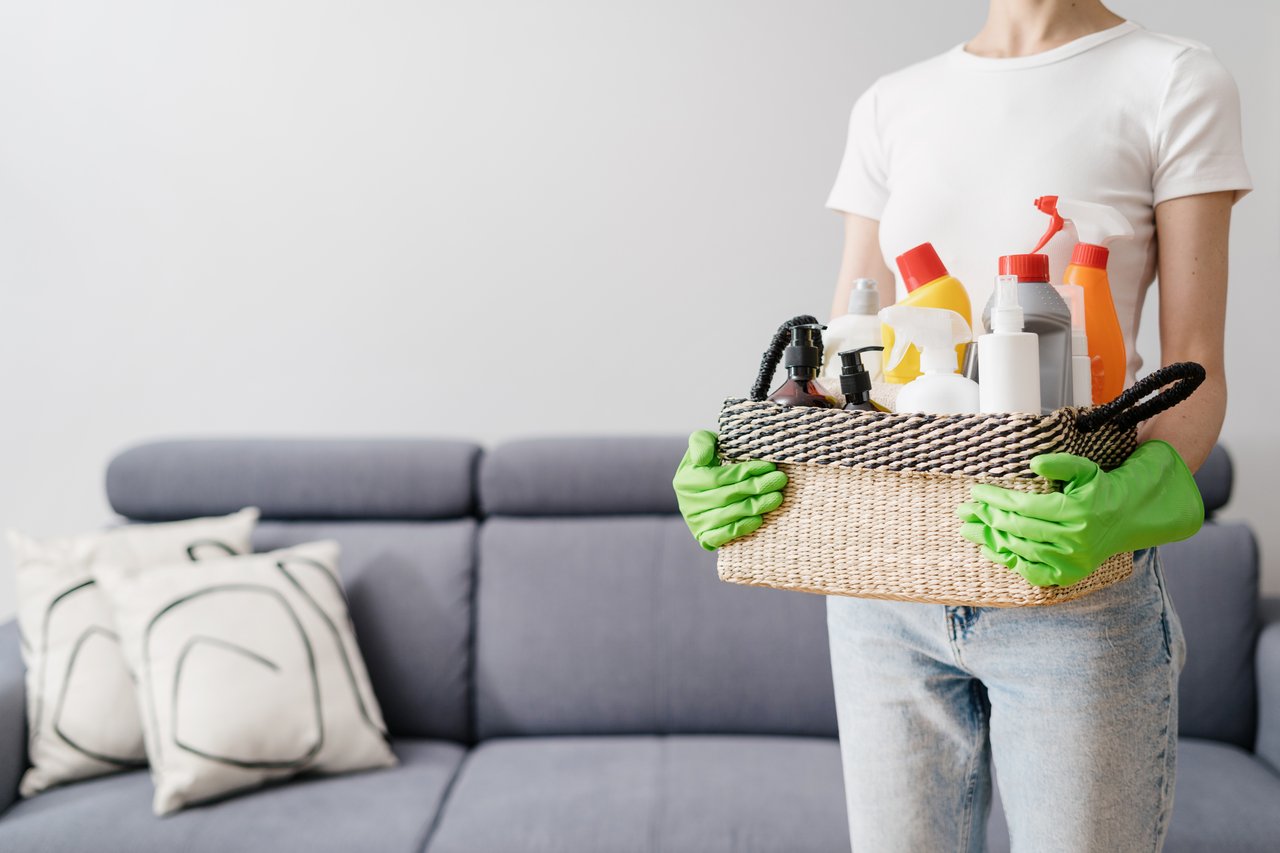 Person holding a basket of cleaning supplies, symbolizing a summer cleaning checklist for a fresh start to the season.