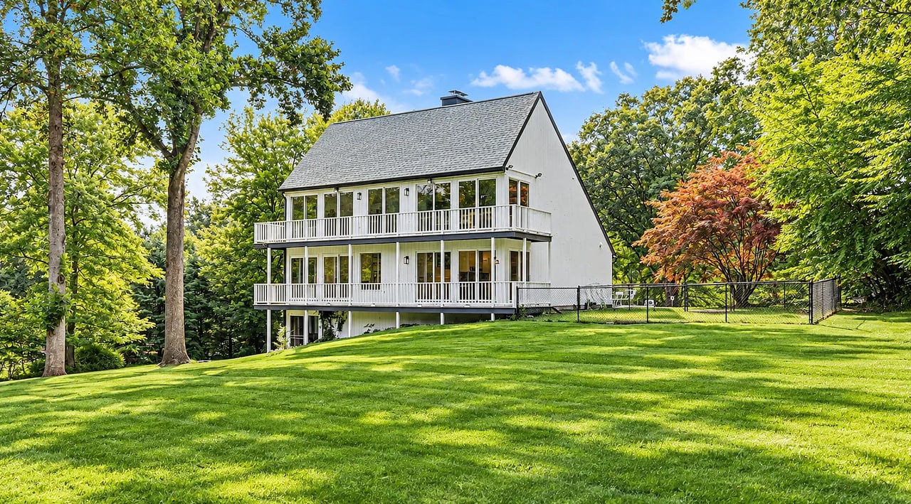 White multi-level house with two balconies above a sloping lawn and fenced yard.