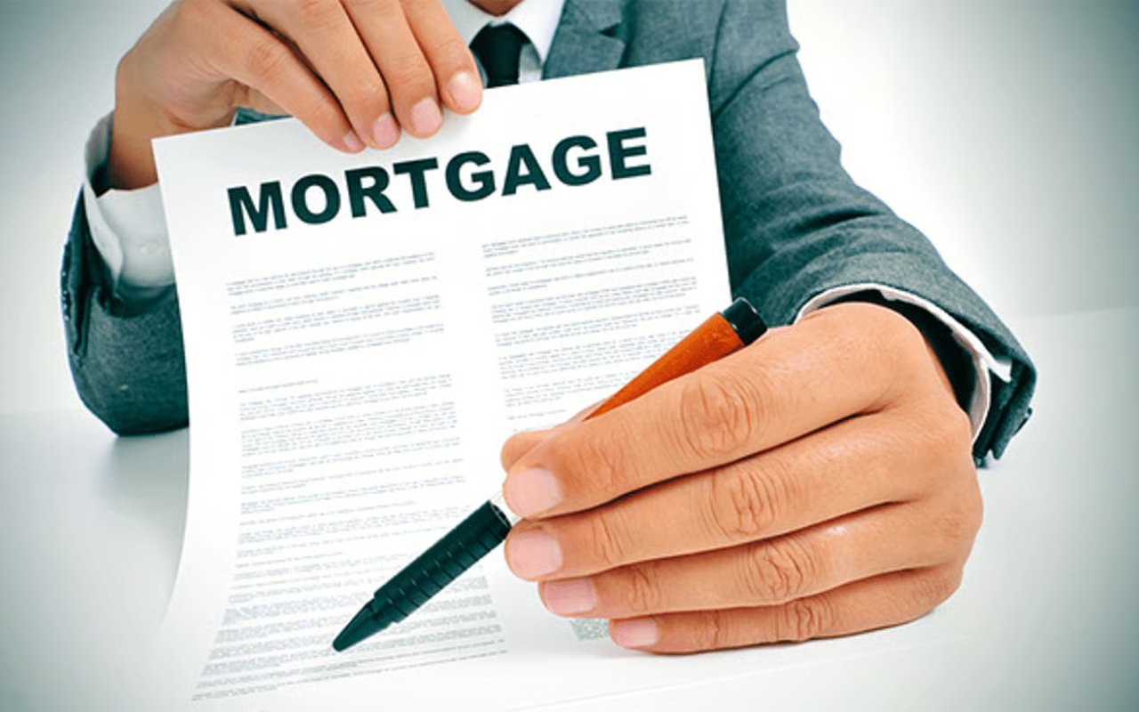 A suited person holds a mortgage document and pen.