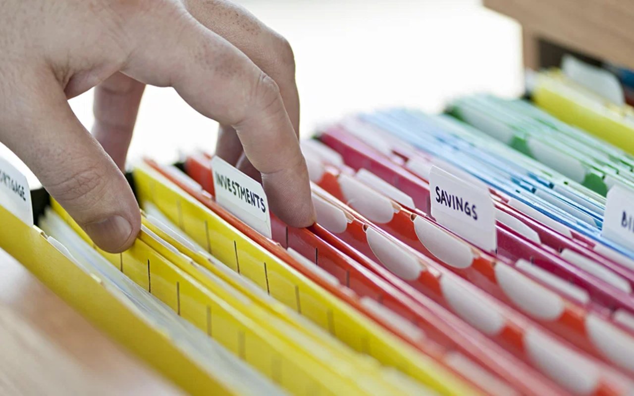 A hand sorts colorful financial folders labeled Investments and Savings.
