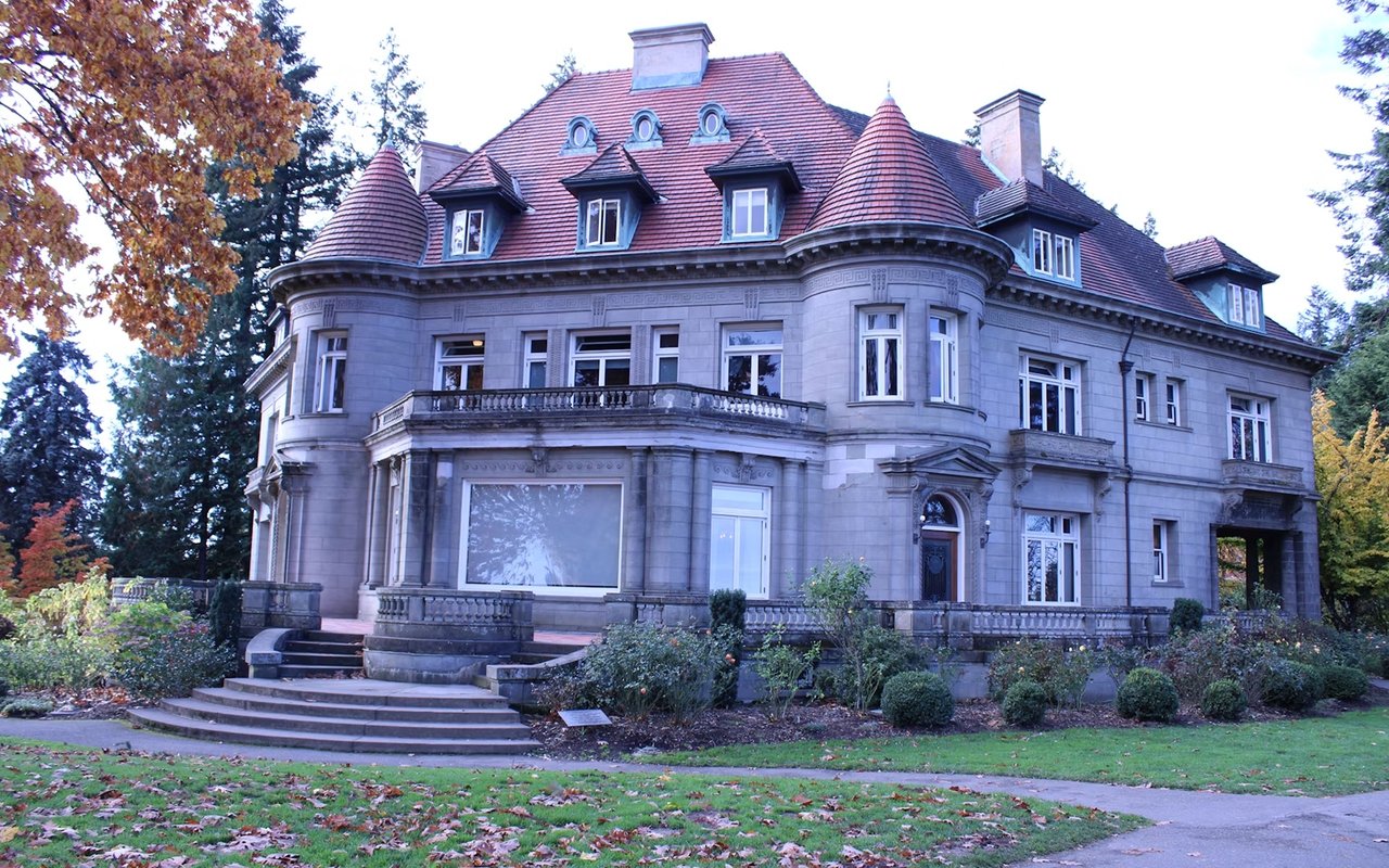 Pittock Mansion’s stone façade, red tiled roof, and turrets framed by autumn trees.