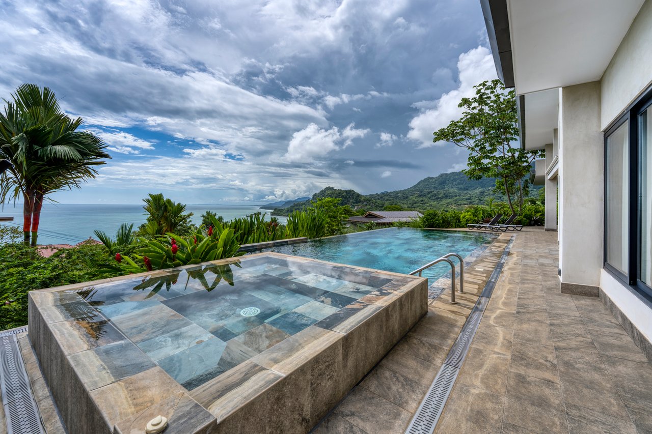 Modern tropical home with a tiled pool terrace overlooking the ocean and green coastal mountains.