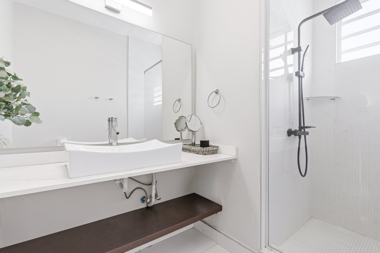 Modern bathroom with a vessel sink, large mirror, and glass-enclosed shower with black fixtures.