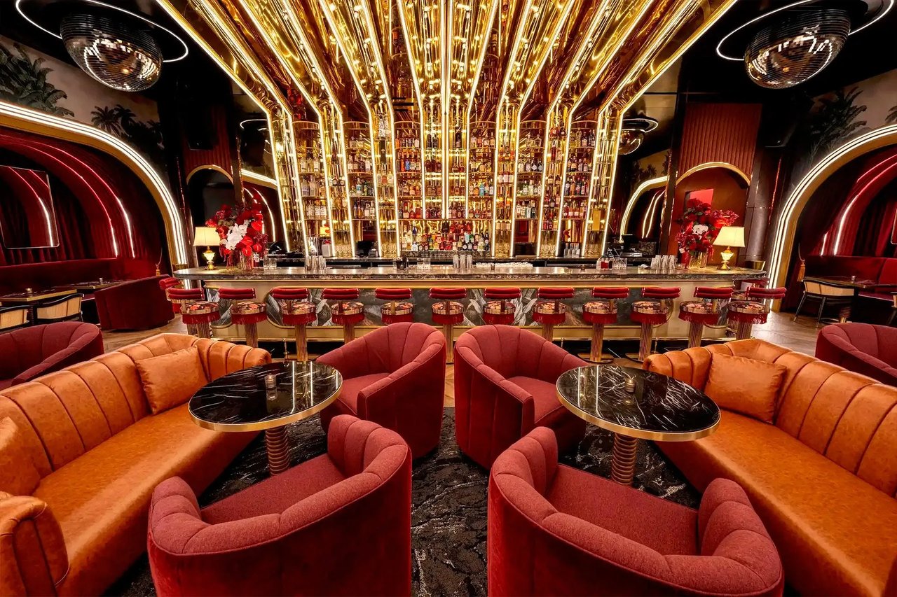 Lavish bar lounge with a glowing liquor display, red velvet chairs, and orange banquettes.