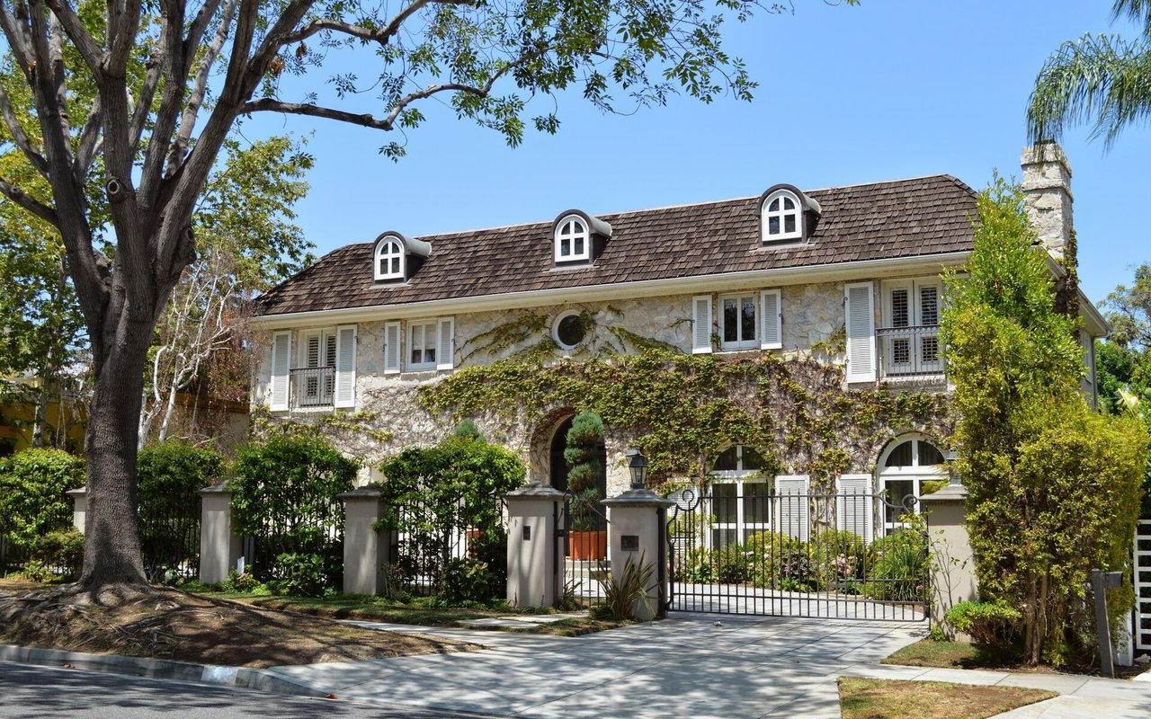 Stone house with ivy-covered walls, three roof dormers, and a gated entrance.