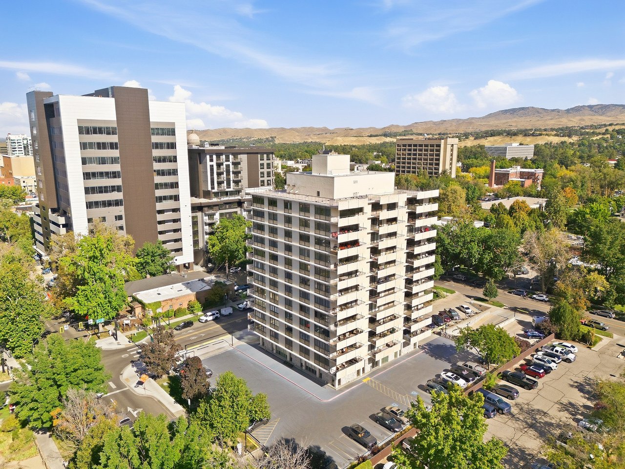 Aerial view of a mid-rise condominium building among downtown buildings, parking lots, and tree-lined streets.