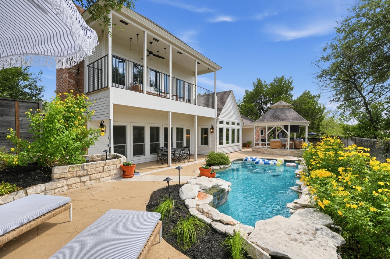 Two-story home overlooking a swimming pool, with a covered balcony, stone patio, and gazebo.