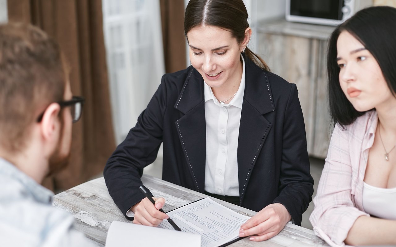 A woman helps a couple complete paperwork at a table.