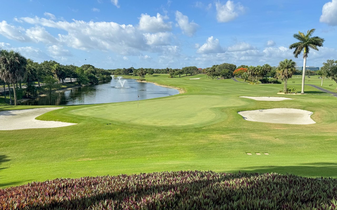 Golf course putting green beside a pond with fountains and white sand bunkers.